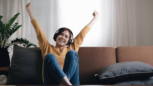 Being energetic. Pretty overjoyed young woman laughing and listening to music and wearing headphones while sit on the sofa and wearing a yellow sweater.