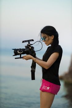 A beautiful brunette girl with a professional camera shoots something on the seashore