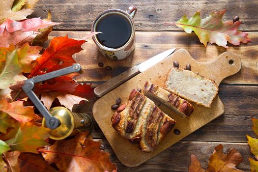 banana cake on the wooden table with orange autumn leaves, copper coffee grinder. High quality photo