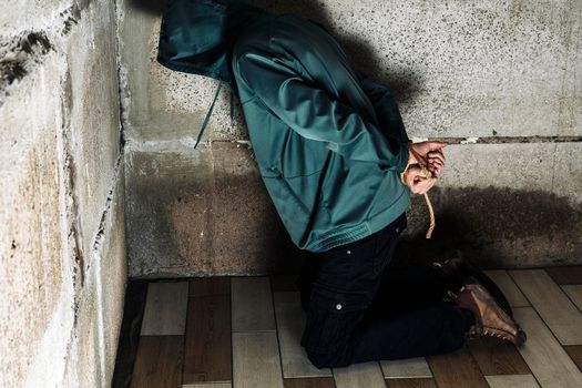 an unrecognizable man in a hood is captured in the basement bound by a rope hand and foot . The kidnapped man is tied up, sitting in the basement. Hands and feet are tied with rope. kneeling on the floor