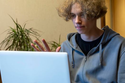 A young guy is chatting in a video chat via a laptop. video call. Remote communication. A happy Caucasian guy waves his hand at the laptop camera. Video call via computer, Communication with family