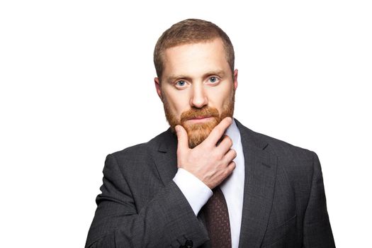 Closeup portrait of serious calm handsome businessman with facial beard in black suit standing, relaxed, touching his face and looking at camera. indoor studio shot isolated on white background.