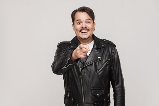 The happiness man, wearing black jacket, having happiness looks, pointing finger at camera and toothy smiling. Isolated studio shot on gray background
