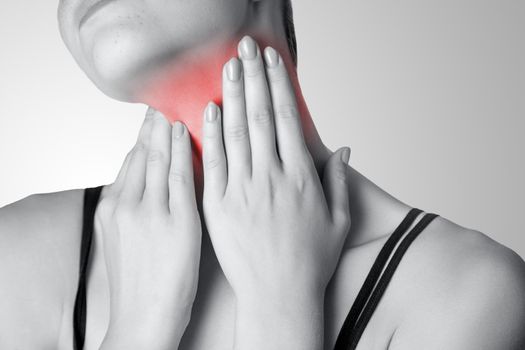 Closeup view of a young woman with pain on neck or thyroid gland on gray background. Black and white photo with red dot.