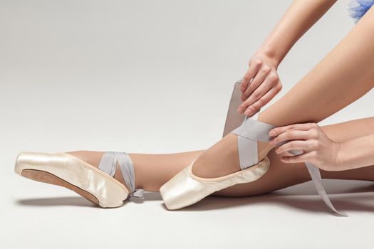 ballerina tying pointe shoes while sitting isolated on white studio background, close-up. indoor, studio shot.