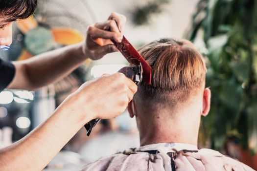 Lifestyle photo barbershop. Young man customer wears face mask, side back rear view. Hairdresser male hand work move comb tool electric clipper. Modern short hair locks cut. Fashion service salon.