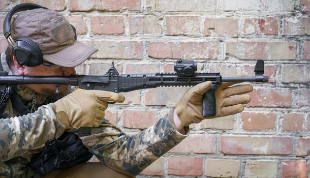 In-service training cycle for civil police troops. Man with gun standing sideways near brick wall during advanced firearms, defence tactics, use of force policy review, officer safety updates.