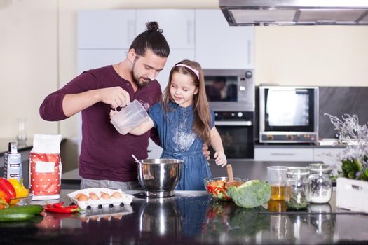 Father teaches his daughter to cook at home in the kitchen.