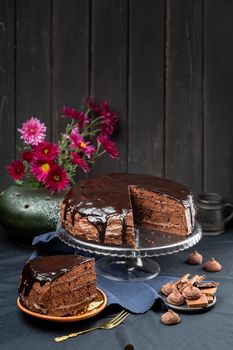 A portion of Delicious Homemade Dark Chocolate Cake Dessert with Ganache glaze topping on the cake stand over dark rustic wooden background