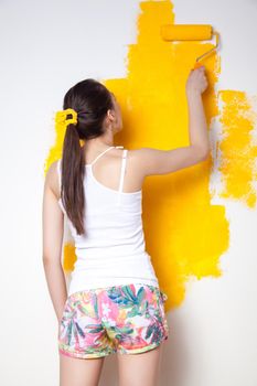 Beautiful young caucasian model in coloured shorts and white shirt and posing holding outrigger in her hands, painting the wall and looking at camera. Studio shot.