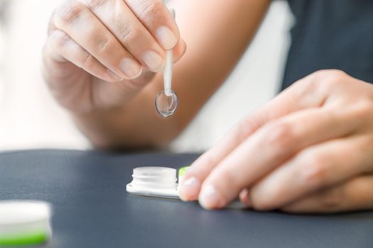 Girl holds the contact lens with tweezers.. Black background, close-up, lower angle