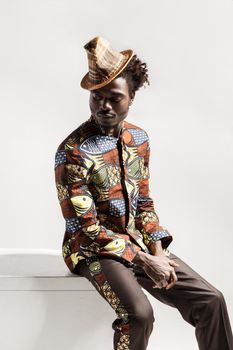 African man in national costume sit on coub . Indoor, isolated on gray background