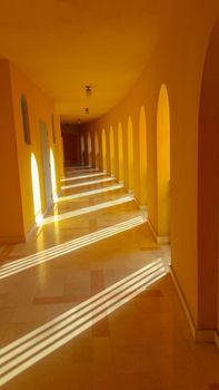 empty long corridor, a hall in orange and the sun's rays from the windows cross it
