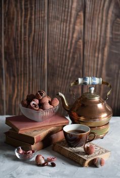 still life with lychee fruit and a vintage copper teapot on the background of a stack of books and a wooden brown background for homely cozy tea drinking and reading,. High quality photo