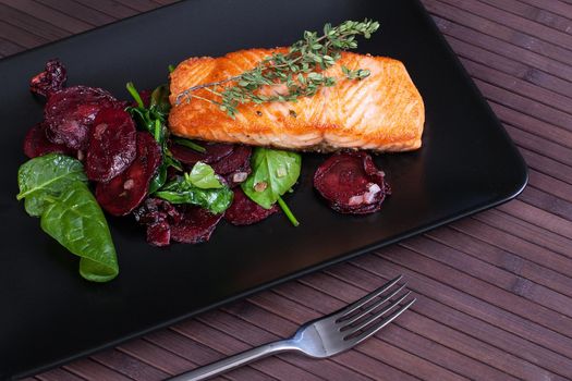 Salmon fillet with baked beetroot on a black plate. Stock image.