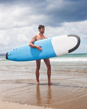 active young surfer holding a surfboard at the beach