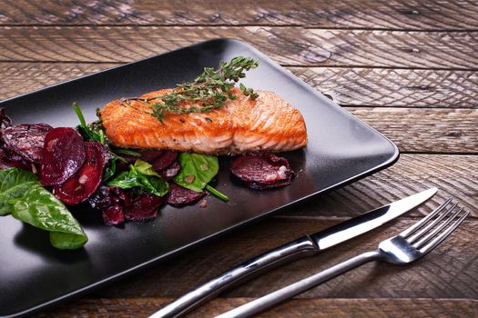 Salmon fillet with baked beetroot on a black plate. Stock image.
