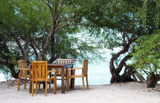 Romantic place with a table on the beach in the shade of trees. Stock image.