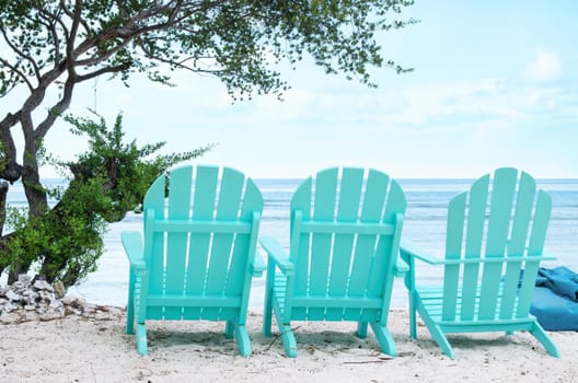 Bright turquoise beach chairs on white sand overlooking the ocean. Stock image.
