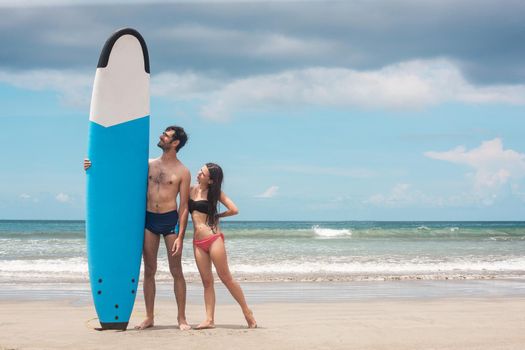 Happy young couple standing with a surfboard on the beach. Stock image.