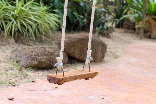 There is a wooden swing in the park for sitting.