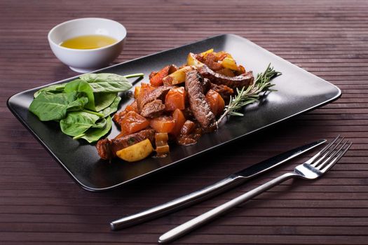Braised veal with eggplant and other vegetables Black plate. Stock image.