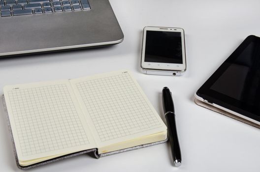 Laptop and notebook on a white table. Stock image.