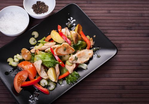 Vegetable salad with chicken on a black plate. Stock image.