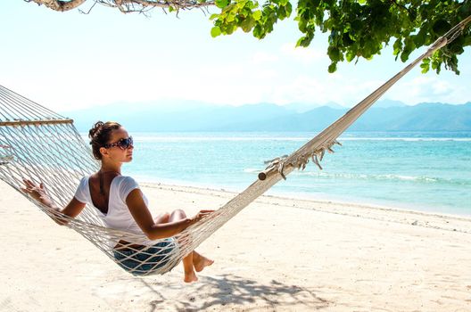 Girl relaxing in hammock on the beach near blue ocean. Bali, Indonesia. Stock image.