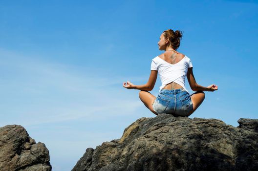 Woman Practicing Yoga sitting on a rock in front of the azure ocean. Stock image