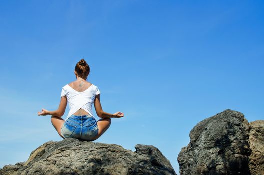 Woman practicing yoga sitting on a rock in front of the azure ocean.