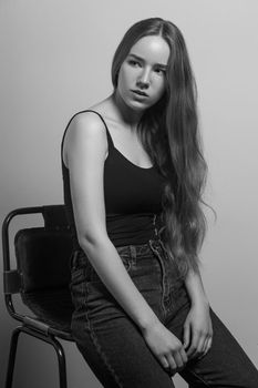 Beautiful woman sit on chair and looking away. Studio shot, isolated on gray background