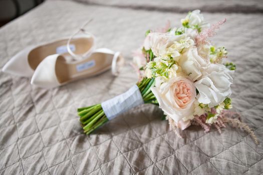 Bridal accessories: beige shoes and bride's bouquet on a bed with pink background