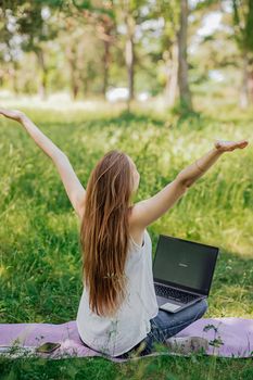 the girl sits outdoors and works at a laptop. she rejoices at the end of the working day. freelance. selfeducation. the concept of remote learning and outdoor work
