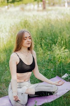 Yoga woman on green grass girl relaxes in the field. Yoga woman in green park girl doing gymnastics outdoors. Meditating woman in meditation in yoga pose practices outdoors