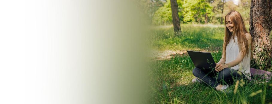 On the banner, a young girl works with a laptop in the fresh air in the park, sitting on the lawn. The concept of remote work. Work as a freelancer. The girl takes courses on a laptop and smiles