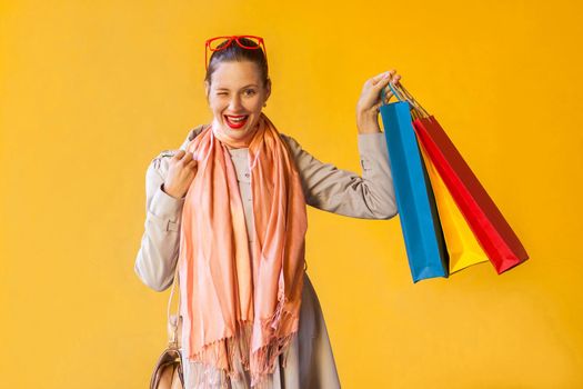 Young adult female model posing in studio. Pretty casual girl with freckles, posing over yellow background. Toothy smiling, wink and flirt and camera and and holding colorful packets. Studio shot