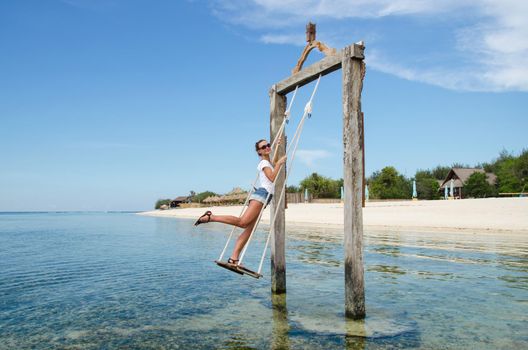 Bali, Indonesia. On the beach a young beautiful girl riding on a swing in the ocean. Stock Image