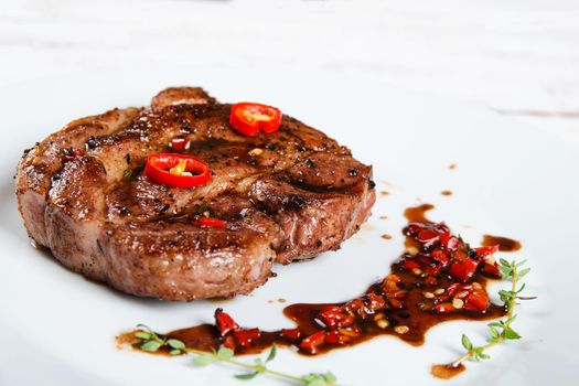 Steak on a white plate with spicy red sauce. Stock image.