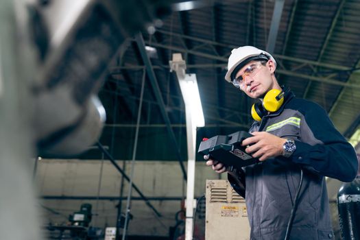 Young factory worker working with adept robotic arm in a workshop . Industry robot programming software for automated manufacturing technology .