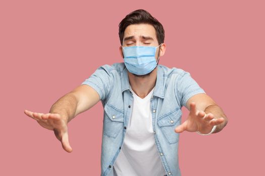Loneless and blindness. Portrait of lost worry man with surgical medical mask in blue shirt standing with closed eyes and try to touching something or find. indoor shot, isolated on pink background.