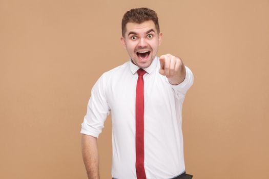 Happy businessman showing finger at camera and toothy smiling . Business people concept, good and bad emotion and feelings. Studio shot, isolated on light brown background
