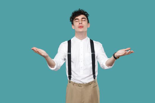 happy in love man raised arms and sending air kiss. Portrait of handsome hipster curly young businessman in classic casual white shirt and suspender standing. studio shot isolated on blue background.