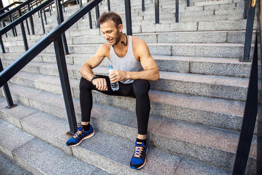 Sportsman with bottle of water is resting and checking his smart watch after running. fitness, sport, exercising and people healthy lifestyle concept.