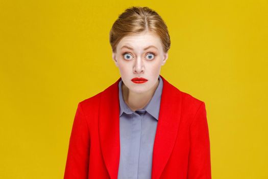 Ginger red head woman in red suit wonder. Studio shot, isolated on yellow background