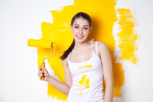 Beautiful young caucasian model in coloured shorts and white shirt and posing holding outrigger in her hands, painting the wall and looking at camera. Studio shot.
