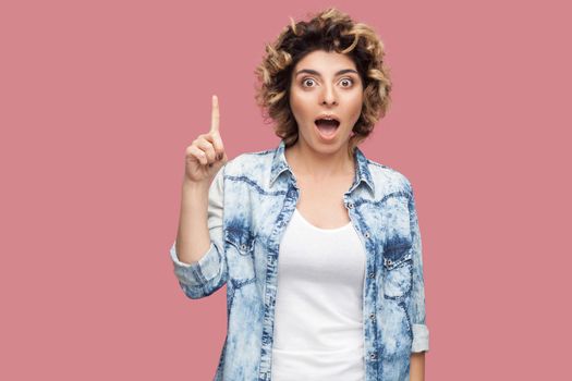 Idea. Portrait of surprised young woman with curly hairstyle in casual style standing and looking at camera with amazed face and idea finger gesture. indoor studio shot, isolated on pink background.
