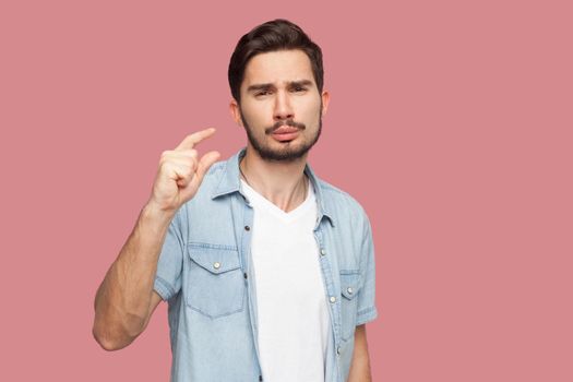 I need a few more. Portrait of hopeful handsome bearded young man in blue casual style shirt standing and looking at camera and begging for something. indoor studio shot, isolated on pink background.