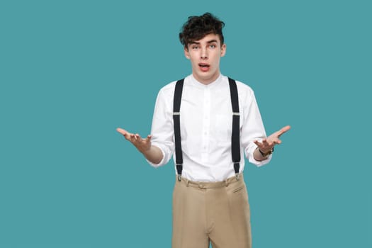 What do you want? man asking and looking at camera. Portrait of handsome hipster curly young businessman in classic casual white shirt and suspender standing. studio shot isolated on blue background.