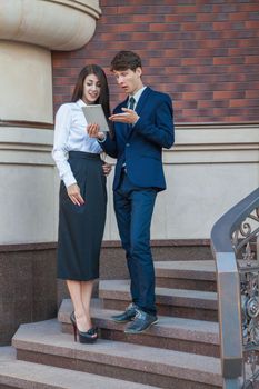 Business people using a digital tablet outdoor. Businessman and Businesswoman standing friendly on steps and using tablet with smile in the city.